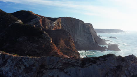 epic aerial view showing group of people hiking on dangerous mountain trail with beautiful ocean mountain landscape in background