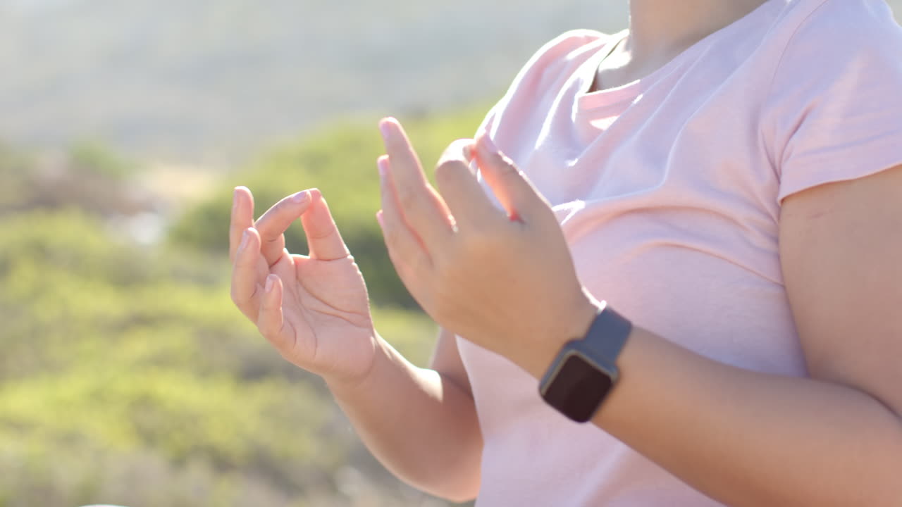 Meditating outdoors, person with smartwatch sitting cross-legged in park