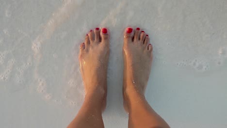 female model standing in the sand having her feet wet by the beach waves