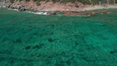 Ruhige-Wellen-Von-Kristallklarem-Blauem-Wasser,-Das-Im-Sommer-Auf-Sardinien,-Italien,-An-Der-Felsigen-Küste-Der-Berge-Plätschert