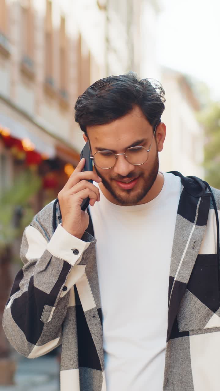 Indian young man tourist on smartphone chatting with friend while walking in the city street