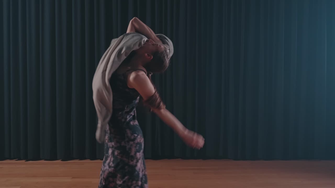 Woman in a black dress dancing emotionally with a fabric prop on stage in front of dark curtains