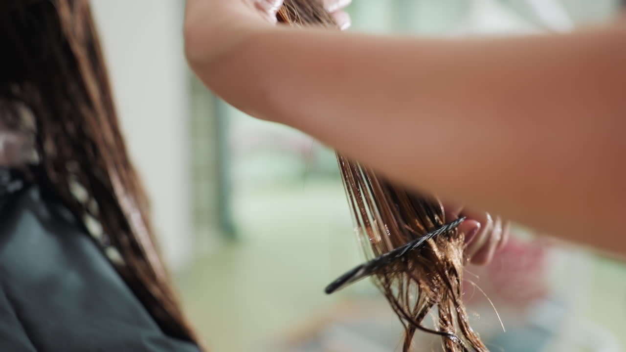 미용사가 가위로 젖은 머리를 다듬는 클로즈업 장면이에요. 부드러운 햇빛 아래 미용실 케이프와 거울이 보이고, 섬세한 손길로 머리카락을 잡고 정확하게 끝을 자르고 있어요. 차분한 분위기의 현대적인 미용실입니다.