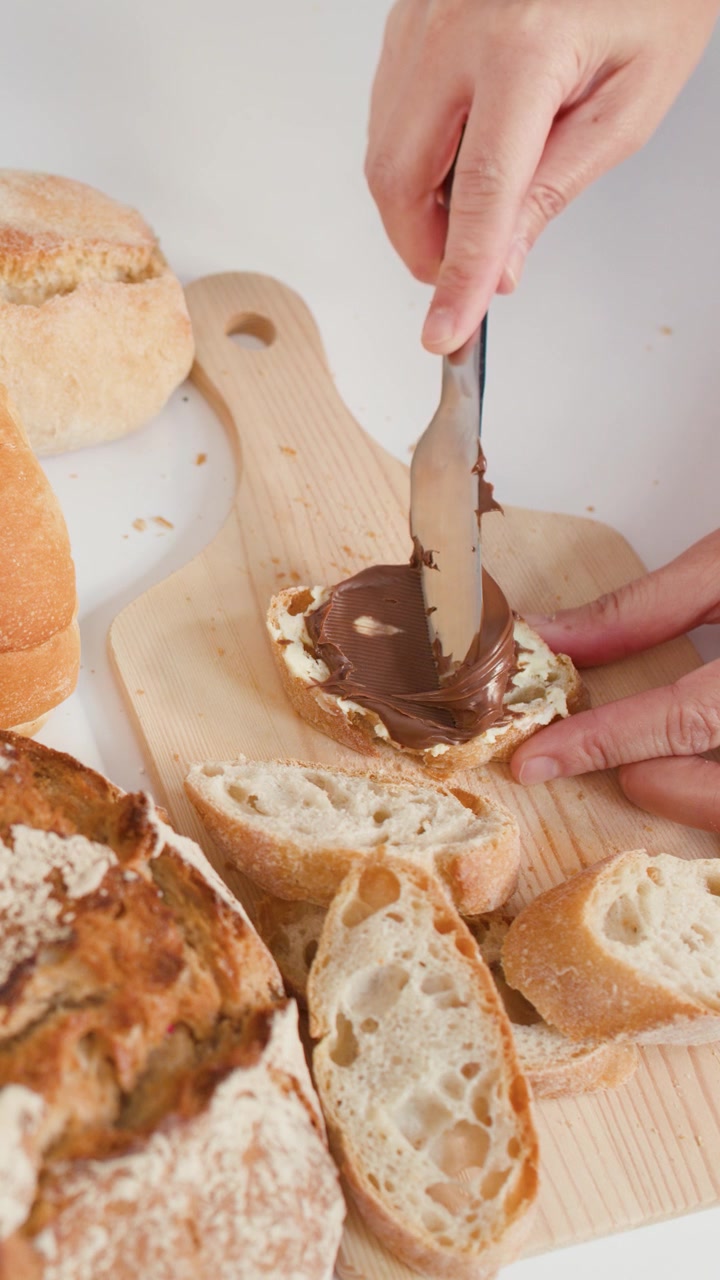 Close-up overhead shot of spreading chocolate cream on bread over a wooden board.