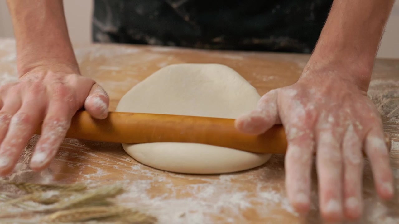 Close-up of Hands Rolling Dough with a Wooden Pin on a Floured Table
