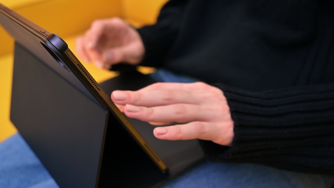 Young content creator using her tablet on yellow sofa. Cozy environment for working from home. Close up typing