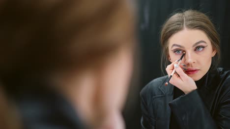 woman applying dramatic eye makeup in front of a mirror