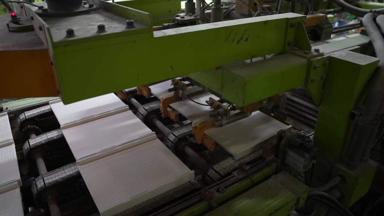 Green hydraulic press forms white ceramic tile sheets on an automated production line