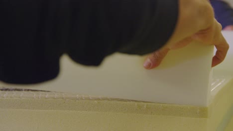 close-up of hands placing foam layer on boxspring in bed manufacturing setting