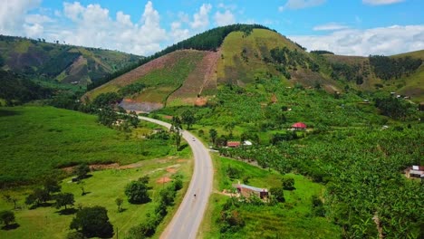 Country-Road-Surrounded-With-Lush-Fields-And-Mountains-In-Uganda---aerial-shot