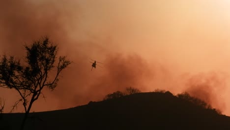 a large wildfire burning in the landscape near los angeles, california, with a helicopter flying overhead, likely involved in firefighting efforts. captures the scale and intensity of the emergency.