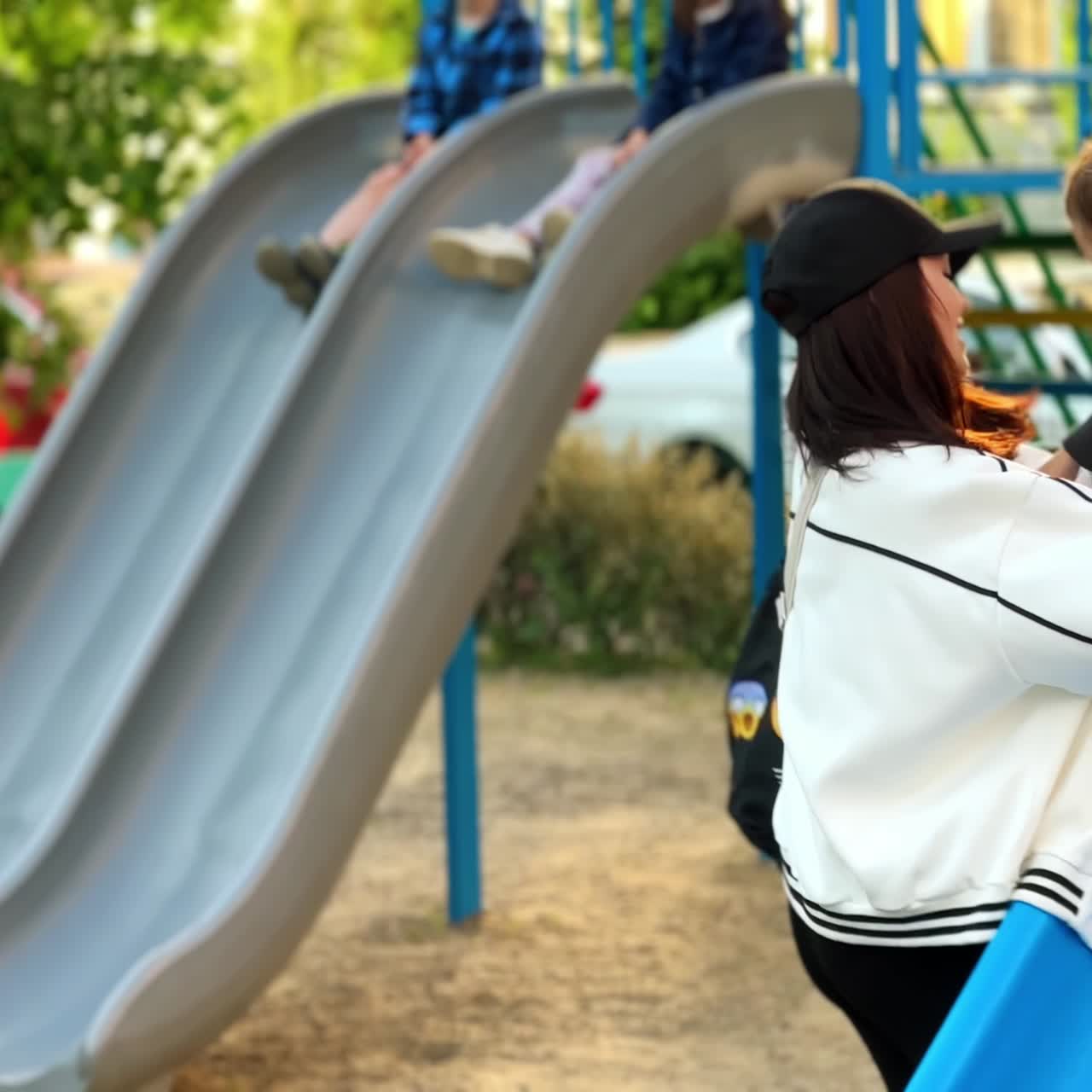 Mother helping her baby to go down from a slide. Kid is excited and wants more. Playground at backdrop