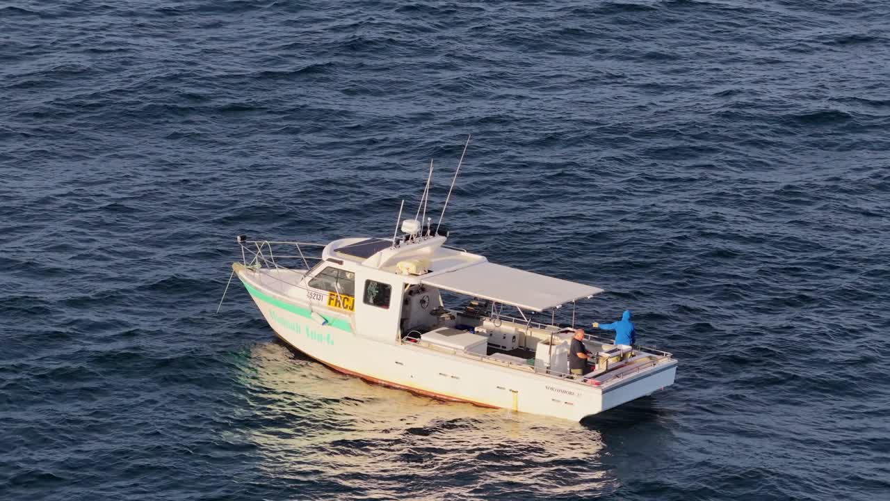 A commercial fishing boat cruises on open ocean waters off Gold Coast, Australia, captured in smooth aerial drone footage during golden hour lighting