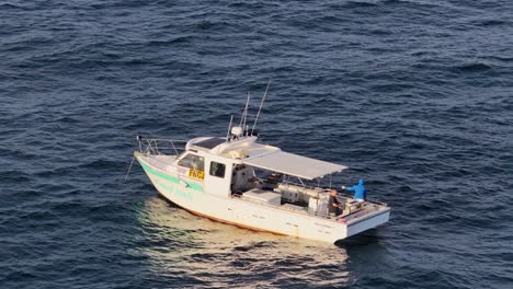 a commercial fishing boat cruises on open ocean waters off gold coast, australia, captured in smooth aerial drone footage during golden hour lighting
