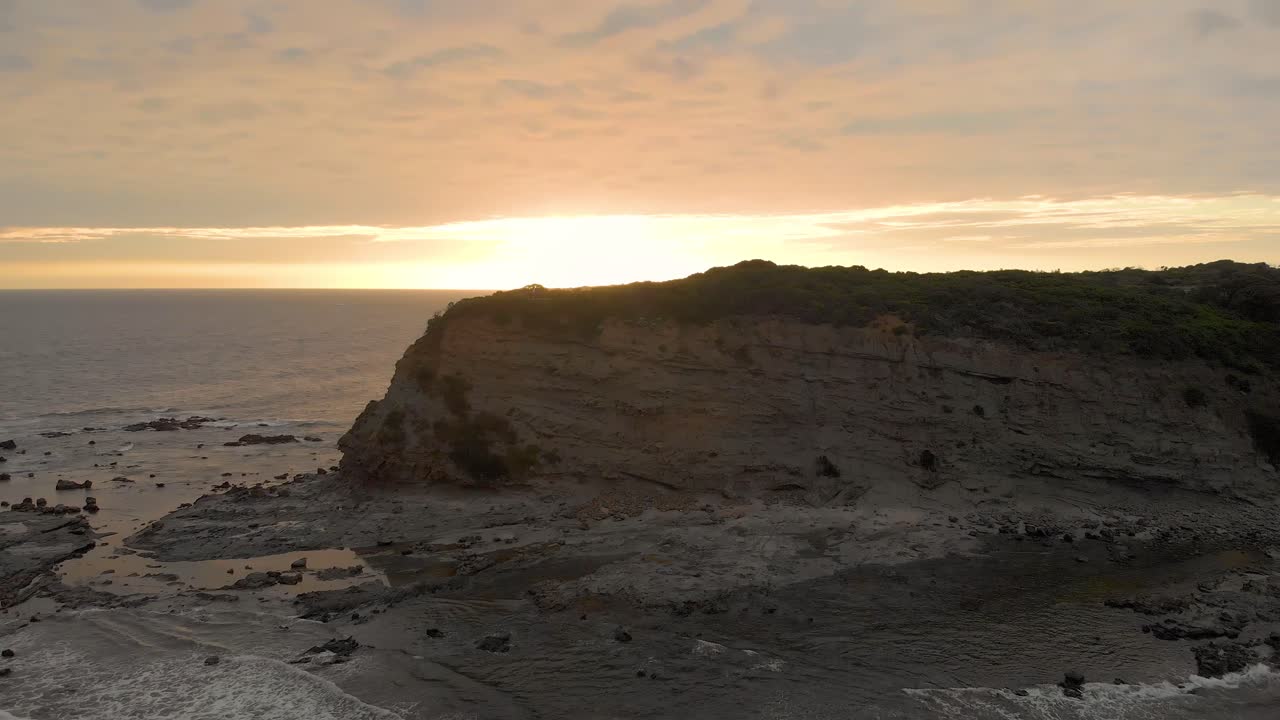 toma aérea volando hacia atrás mientras mira los escarpados acantilados en la costa de bass victoria australia con la puesta de sol en el horizonte
