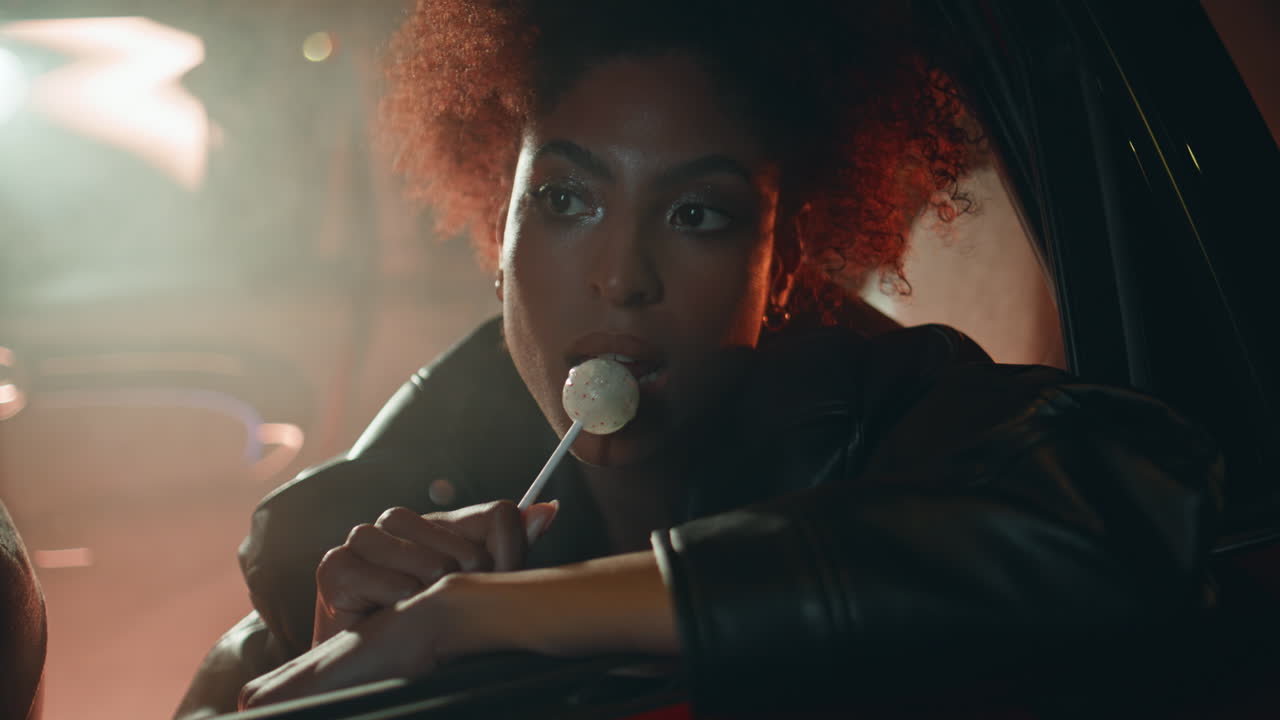 Confident woman eating candy leaning on car window under night light closeup
