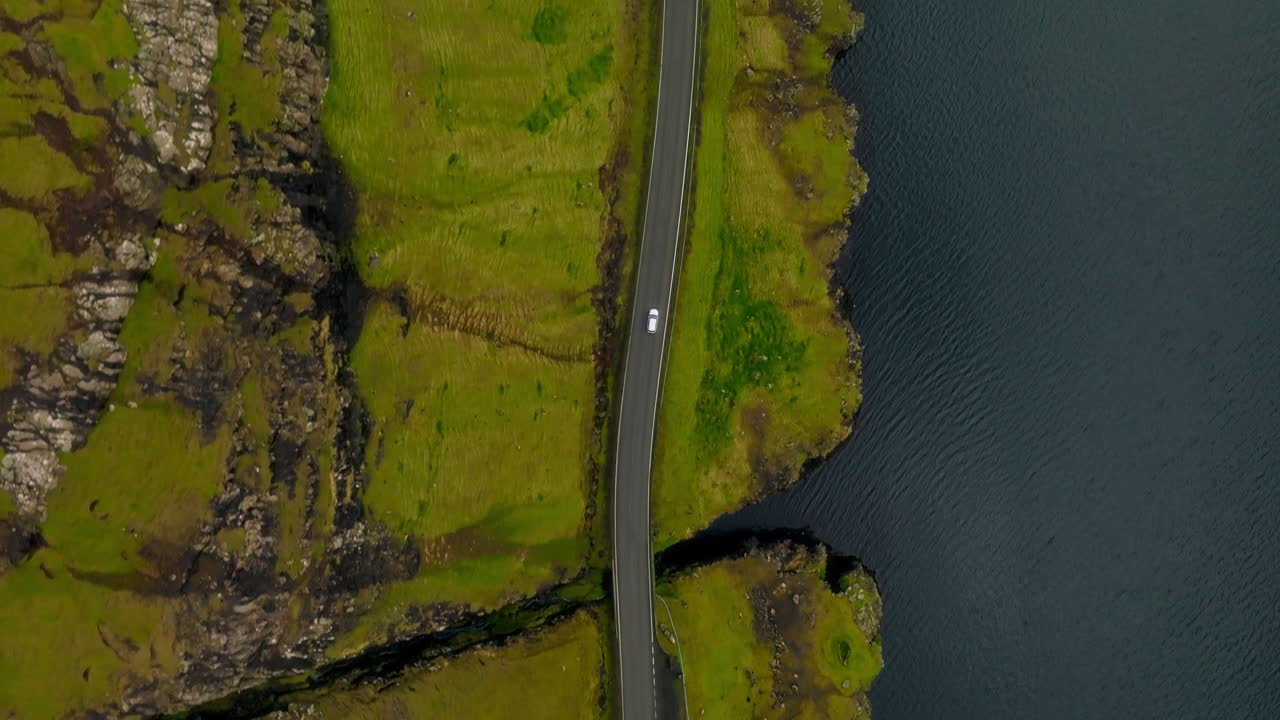 A scenic road between grassy cliffs and a blue lake in the Faroe Islands