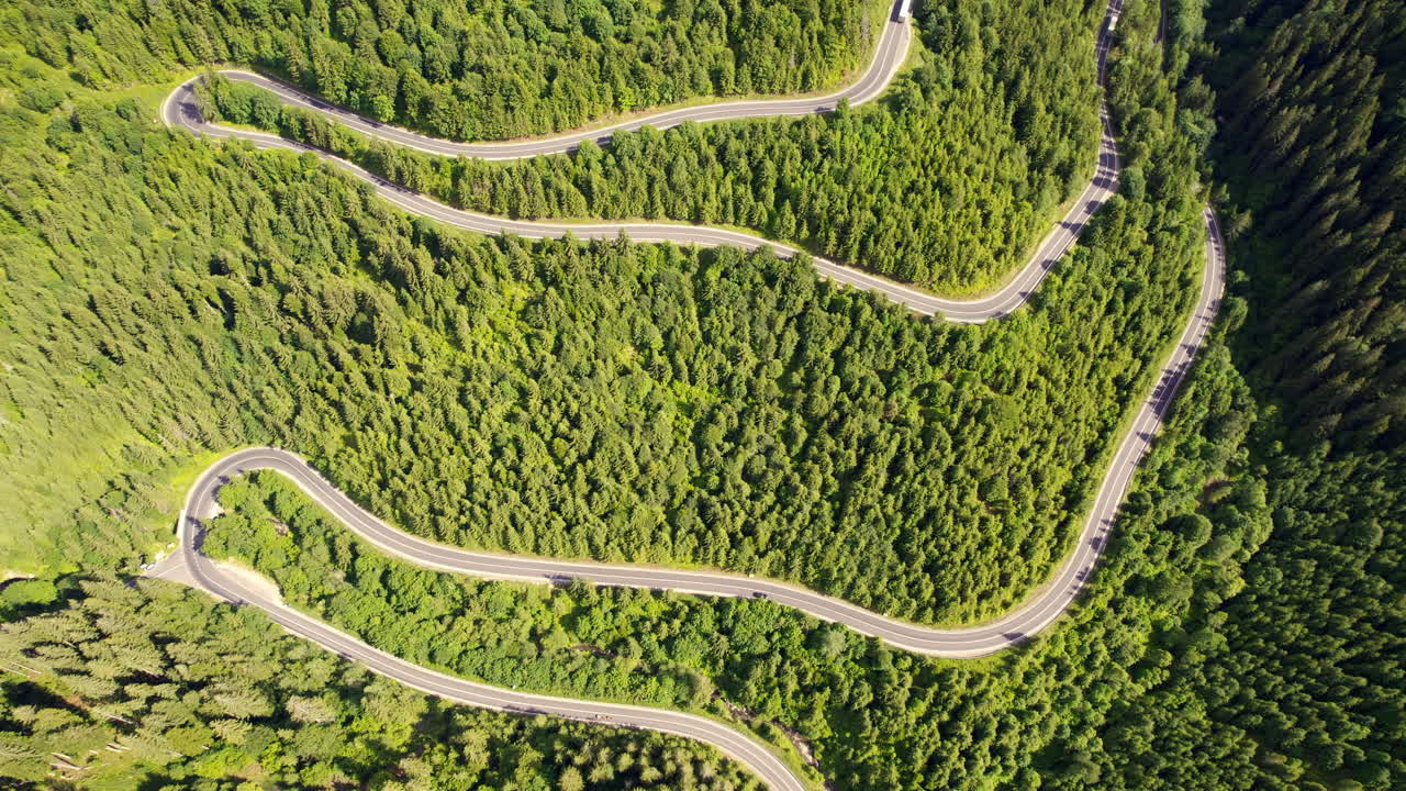 Aerial drone view of nature in the Carpathians in Romania. Road with moving cars, hills covered with lush forest