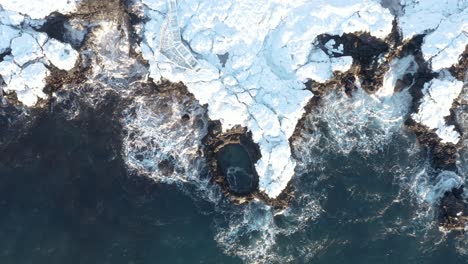 top down aerial at brimketill rock pool with coast covered in snow, iceland