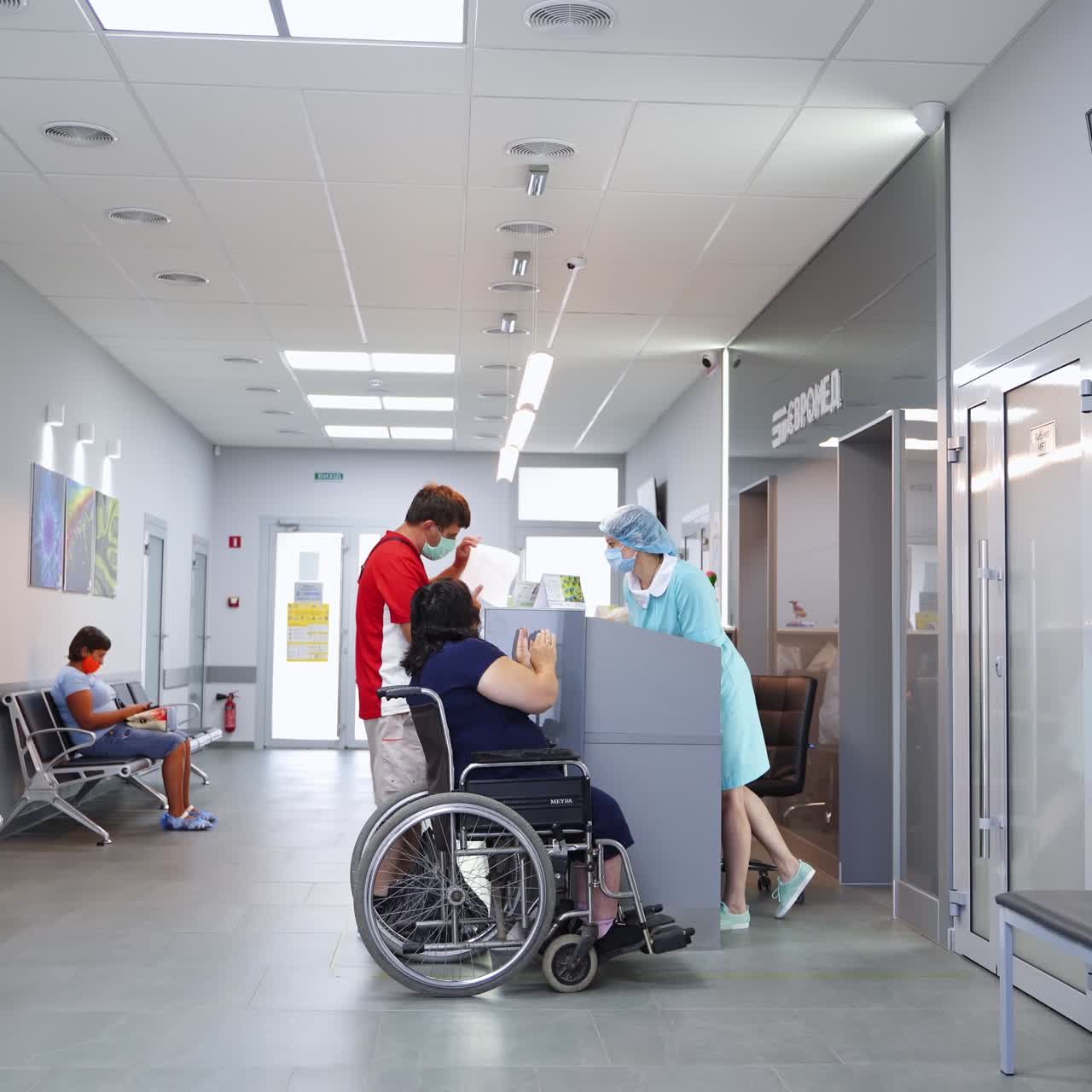 Big hall in the modern hospital. Patients waiting for their turn to the doctor. Woman in wheel chair is at the reception