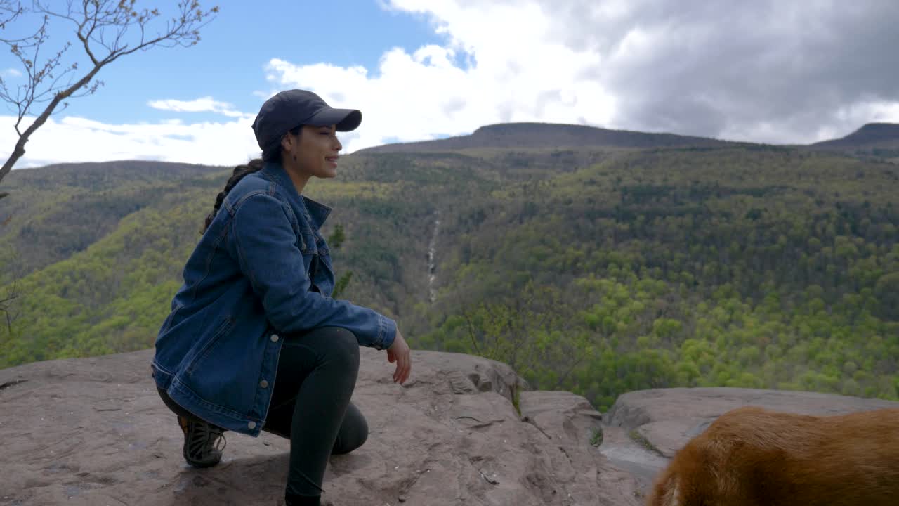 하이킹 트레일 뷰포인트를 바라보는 폭포를 바라보는 젊은 여성은 밝은  ⁇ 빛의 절벽을 바라보는 폭포를 바라보는 시니어 행복한 개와 함께 웃고 있습니다.