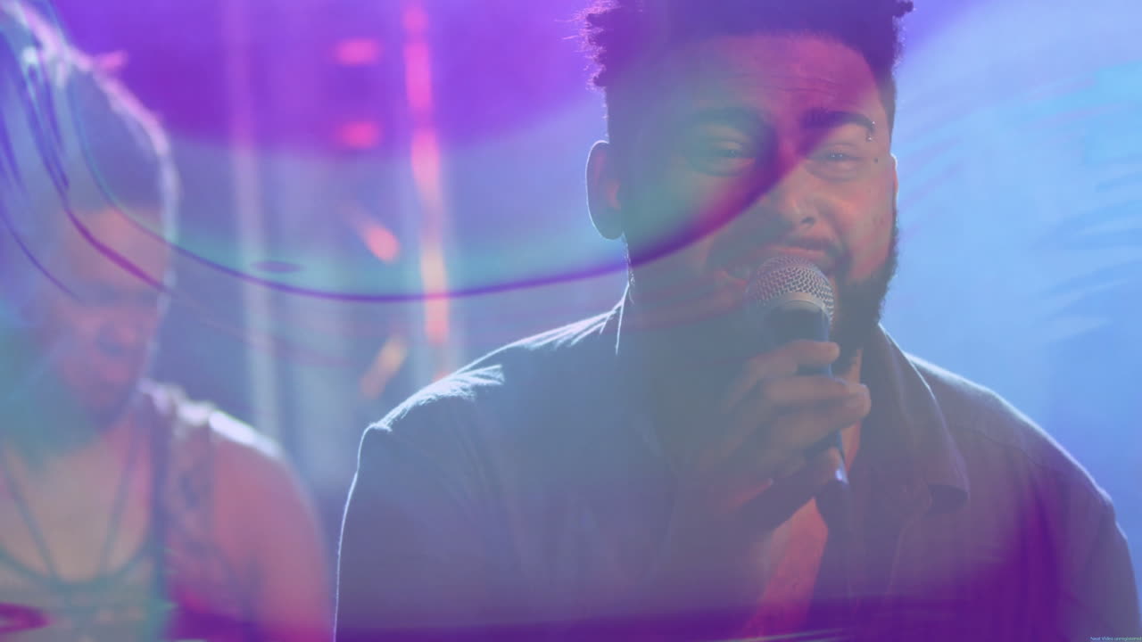 Bearded singer singing into mic and guitarist strumming on stage with motion waves in music