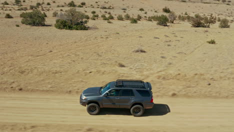 close aerial tracking suv driving on dirt road through open desert terrain