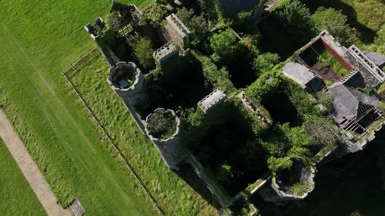 Castle Saunderson, County Cavan, Ireland, September 2022. Drone in Bird's Eye view ascends and circles ruined overgrown castle with green lawns outside, background wide landscape view with cloudy sky.