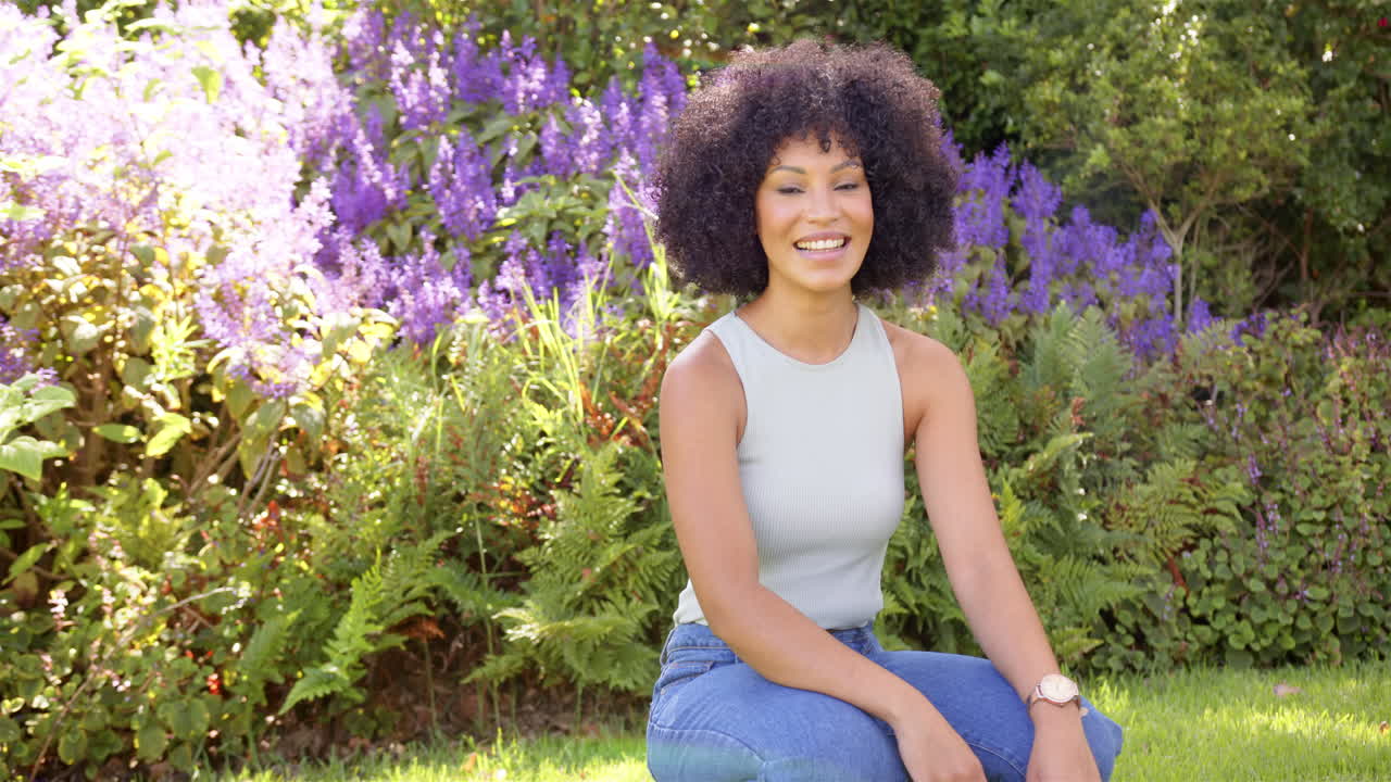 Smiling woman sitting in garden with purple flowers, enjoying sunny day