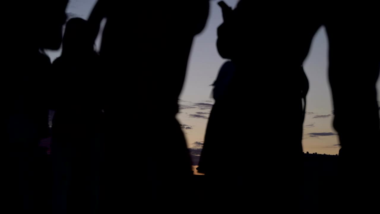 여름 저녁에 도시 공원의 개념과 건강한 라이프 스타일: 해가 지는 하늘 배경에서 산책하는 사람들의 실루, 지나가는 사이클리스트, 스케이트 선수 및 스케이트 보더, 낮은 각도 시야 타임 스 루프