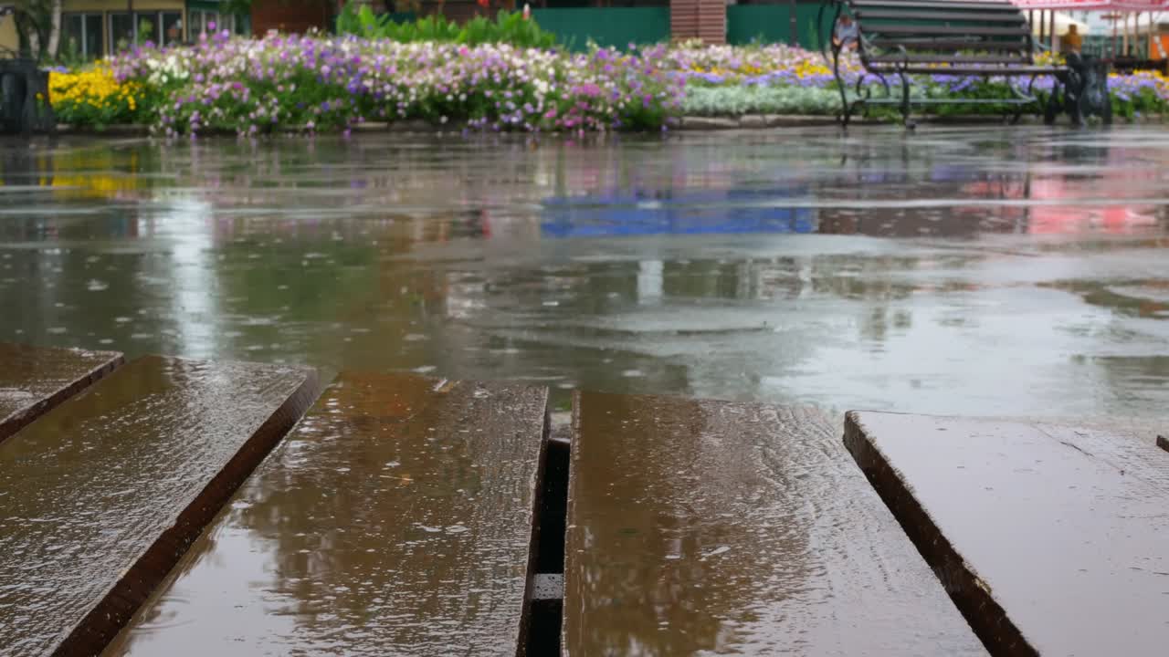 도시 공원에서 비가 내리면, 방울이 테라스의 나무 바닥과 도로의 아스팔트에 떨어집니다. 도시에서 나쁜 날씨, 당신은 테라스에서 비에서 숨을 수 있습니다.