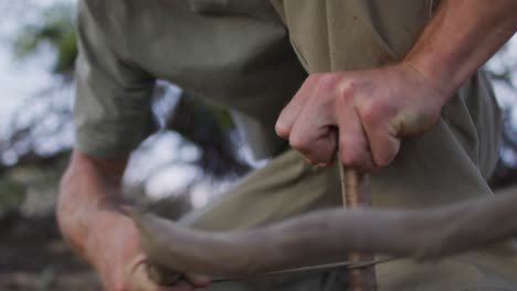 Bearded-caucasian-male-survivalist-using-fire-bow-and-fire-drill-at-camp-in-wilderness