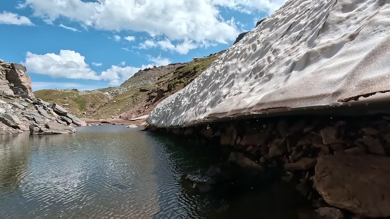 Melting glacier edge touches a cold alpine pond surrounded by rocky slopes in Alpe Veglia Natural Park, Italian Alps