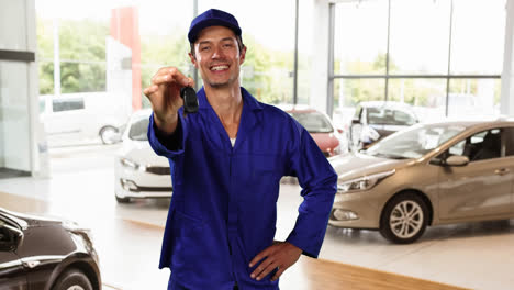 Kaukasischer-Arbeiter-Mit-Blauem-Überwurf-Und-Hut-In-Einem-Autohaus,-Der-Schlüssel-Zum-Auto-Gibt-Und-Lächelt