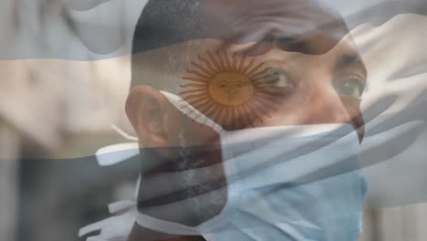 Animation-of-flag-of-argentina-waving-over-man-wearing-face-mask-during-covid-19-pandemic