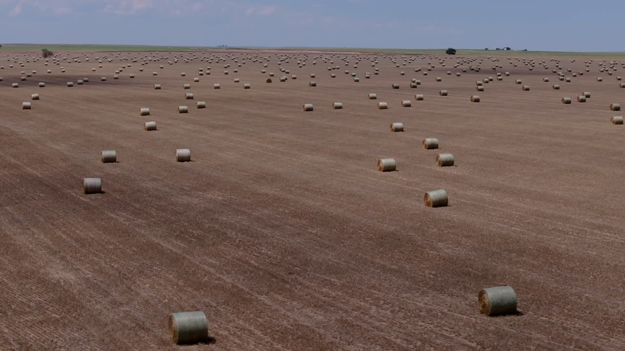Flat Kansas farmland with scattered hay bales under wide sky, aerial tracking right, backdrop