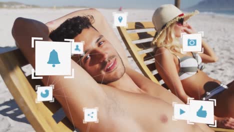 Animation-of-social-media-icons-over-couple-in-deckchairs-on-beach