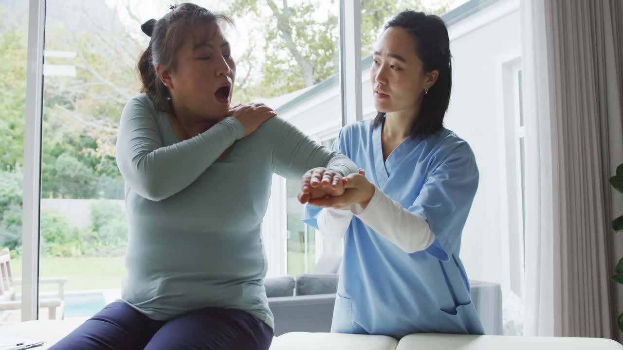 아시아 여성 물리치료사가 수술 중 여성 환자를 치료하면서 팔을 움직이고 있습니다.