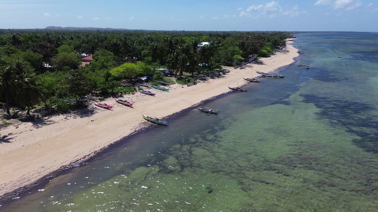 Aerial view of traditional Bangka boats anchored along a tropical shoreline with clear water and sandy beach surrounded by lush green vegetation on Bantayan Island Philippines Southeast Asia