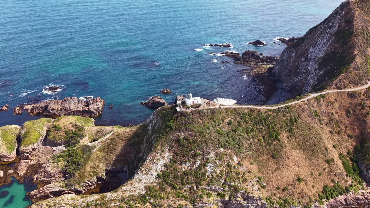 Drone orbit around Nugget Point lighthouse showing rocks, vast ocean and contrasting sea colors