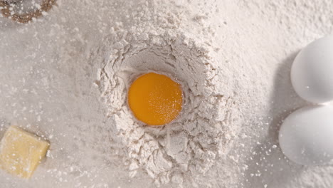 raw egg yolk falling into a pile of white flour making a hole - table top view, slow motion