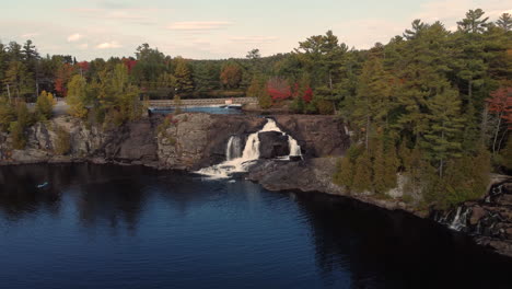 Drohne,-Die-Sich-Im-Herbst-In-Bracebridge,-Ontario,-Kanada,-Mit-Damm-Und-Brücke-In-Der-Nähe-In-Richtung-Muskoka-High-Falls-Nähert