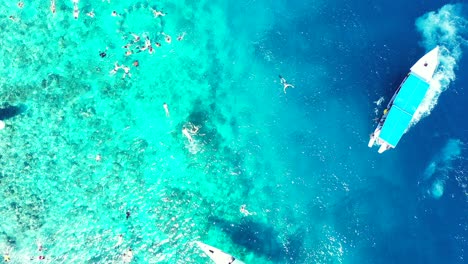 group of people tourists exploring beautiful coral reef in the crystal clear turquoise water, tour boat floating in the calm sea