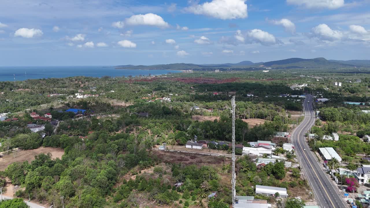 Aerial view of an antenna tower leads into a scene of a main road where vehicle movement allows for a strong presence of greenery on both sides. emphasising the road's role within a residential area.