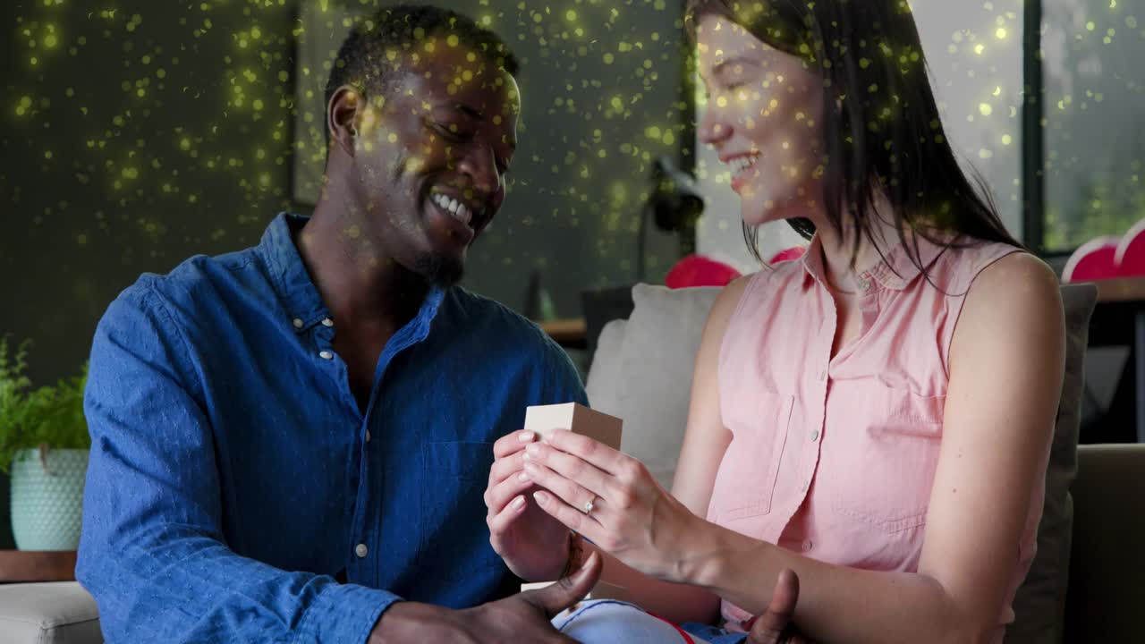 Man handing gift box, woman lifting lid, reacting, golden sparkles enhancing reveal for marketing