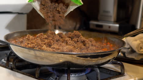 pouring vegan vegetable meatless crumbles into sauce in frying pan, close up