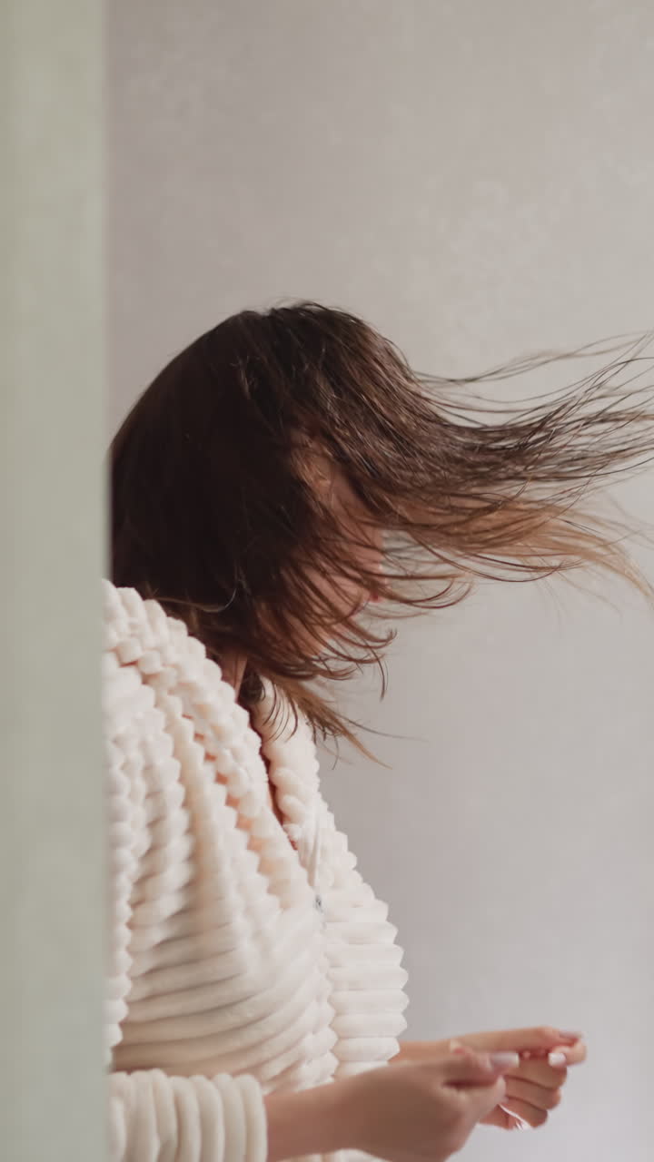 화장실에서 거울을 반사하는 음악에 여성이 움직입니다. 은 머리카락을 가진 젊은 갈색 여성은 샤워 후 음악과 함께 느린 동작을 즐기고 있습니다.