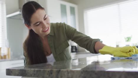 caucasian woman wearing rubber gloves and cleaning table at home