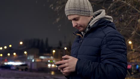 Kaukasischer-Mann-SMS-Am-Telefon-In-Der-Stadt-An-Einem-Kalten-Winterabend