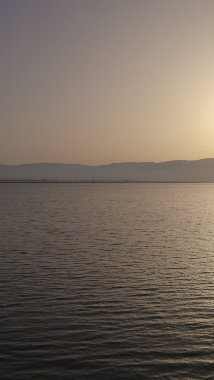 Vertical video of a lonely white trailer parked silhouette on one of the sand dikes separating the Dead Sea